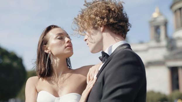 Beautiful couple of newlyweds look at each other. Action. Beautiful couple of newlyweds passionately look at each other. Newlyweds pose on windy sunny day in summer city.