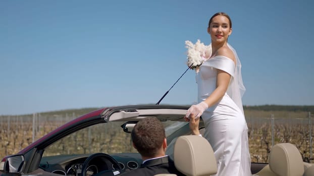 A young bride looks out of the car. Action. A model in a white dress with red lips holds a wedding bouquet in her hands and poses against a blue sky. High quality 4k footage