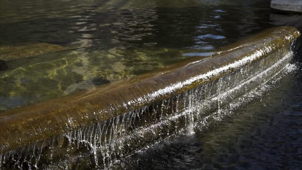 Detail of an old granitic fountain with flowing water in a sunny day. Close up for the stone fountain with the water running over the edge.
