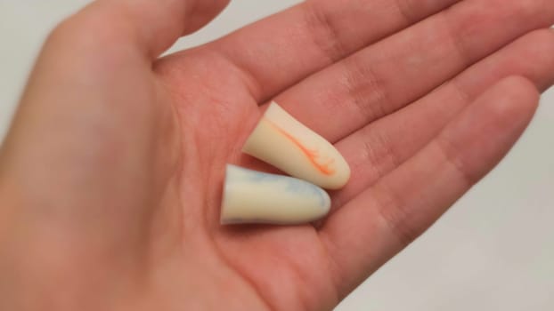 Close up of woman holding ear plugs in her fingers on white background. Pressing soft and soundproof earplugs in female young hands.