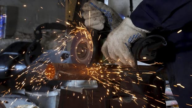Heavy industry worker cutting steel with angle grinder, high-speed video. Worker with angle grinder and protective gloves cutting metal, generating hot sparks.
