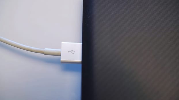 Process of charging device with a white USB cable. Close up of male hands removing the white USB cable from a USB connector inside a laptop or computer.
