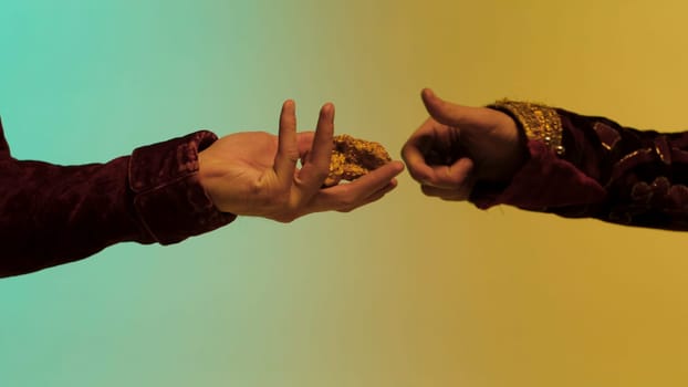 Eastern man taking a piece of gold nugget from another man, hands isolated on colourful background. Close up for man taking piece of gold ore from hands of another man.