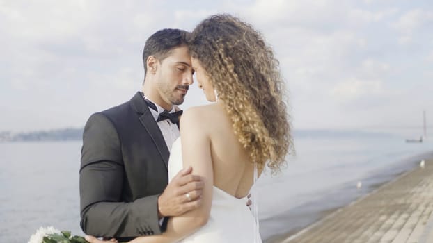 Beautiful bride and groom standing on the summer embankment. Action. Romantic young family couple on their wedding photosession