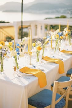 Long festive table with bouquets of flowers and yellow napkins on plates. High quality photo