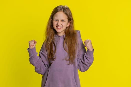 Young preteen child girl kid shouting, raising fists in gesture I did it, celebrating success, winning, birthday, lottery jackpot goal achievement. Little cute children isolated on yellow background