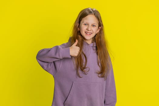 Like. Happy young preteen child girl kid looking approvingly at camera showing thumbs up, like sign positive something good, positive feedback great news. Children isolated on studio yellow background