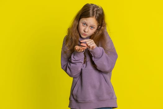 Need some more, please give me. Young preteen child girl kid showing a little bit gesture with sceptic smile showing minimum sign, measuring small size, begging help. Children on yellow background