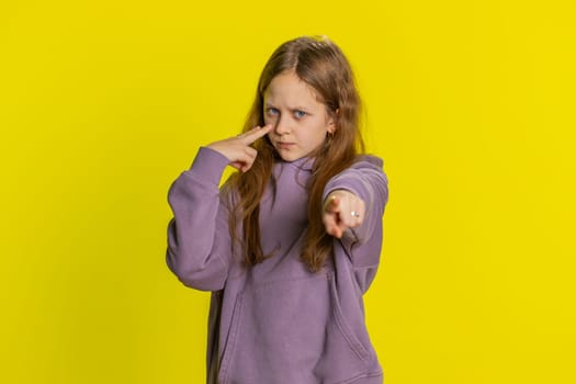I am watching you. Young little redhead school girl pointing at her eyes and camera, show I am watching you gesture, spying on someone. Preteen female child kid isolated on studio yellow background