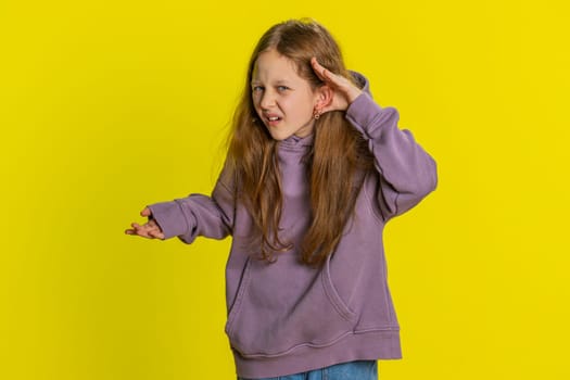 I cant hear you. What. Child girl kid trying hear you, looking confused and frowning, keeping arm near ear for louder voice asking to repeat to hear information deafness. Children on yellow background
