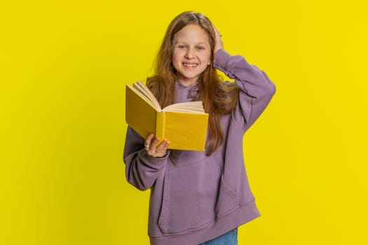 Happy relaxed smiling preteen child girl kid reading funny interesting fairytale story book, leisure hobby, knowledge wisdom, education, learning, study, wow. Children isolated on yellow background
