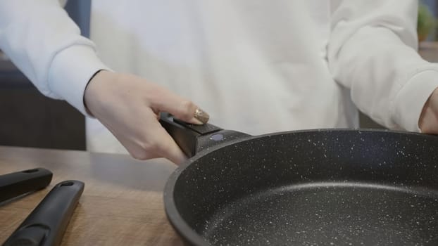 Woman holding modern frying pan. Action. Close-up of woman advertising new frying pans. Woman removes handle from frying pan.