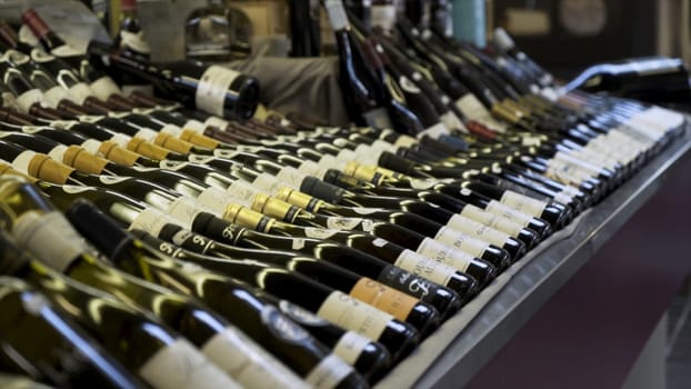 Close up for rows of wine bottles in the shop, luxury alcohol concept. Glass bottles of red and white wine on wooden shelves in private winery collection.