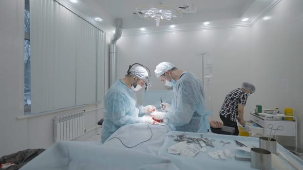 Operating room during operation with two surgeons. Action. Side view of operation under anesthesia by two surgeons. Professional surgeons in process of operating.