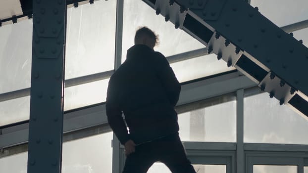 Guy dancing hip hop on bridge. Action. Cool dance in modern style of street dancer. Young man dances in modern style at steel beams of building.