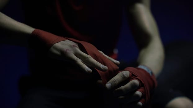 Close-up of boxer's hand. Close-up boxer ties injured hands with red ribbon in dark locker room, preparing for training.