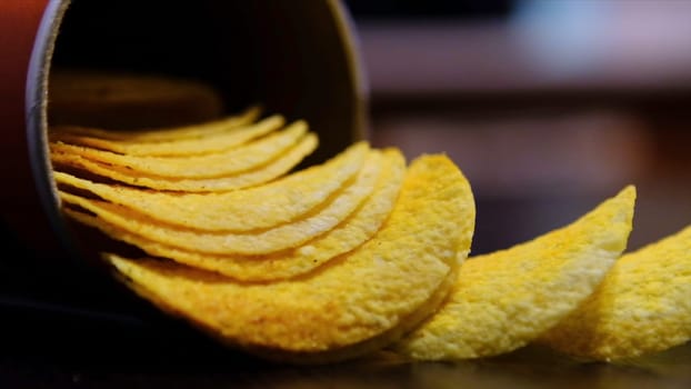 Close up of potato chips put out of can on the table on blurred background. Hand taking delicious snack, concept of unhealthy diet.