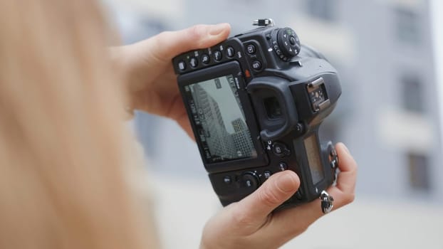 Close-up of woman and professional camera screen. Action. Female photographer shoots residential buildings with professional camera. Camera screen during street shooting.