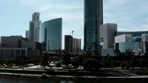A built-up city under the bright sun. Stock footage. Huge glass offices and residential buildings standing next to the lake and walking areas. High quality 4k footage