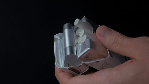 Man's hand pulling up a sigarette from box. Get sigarette from pack closeup. Closeup of a man pulling a nail out of a pack of cigarettes. Box of cigarettes. Hand takes a cigarette out of pack 4K