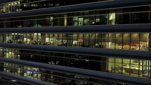 Close up for exterior of modern office building corner with lighted windows and people inside. Aerial of the downtown office building corner at night, lighted windows background.