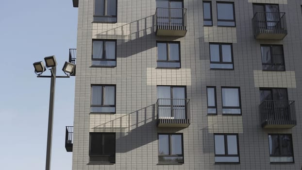 Bottom view of residential new building made of white bricks. Fragment of a white brick new apartment house with balconies and street lanterns against a clear sky.