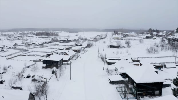 Aerial view of snow covered roofs of wooden houses. Clip. Small winter village on a heavy cloudy sky background