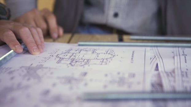 Close up view on engineer hand pointing at technical drawings. Men hands indicating some details in papers, blueprints with building project