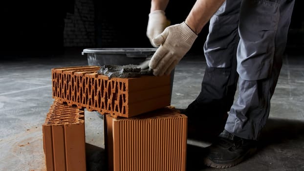 Close up of an industrial worker putting cement on the brick for construction work. Hands of a man putting mortar on red brick, materials and construction concept.