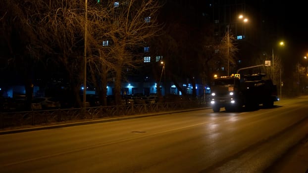 Night city street with a big truck transporting military tank. Concept. Empty road and driving vehicle
