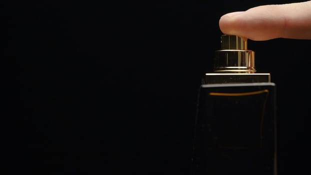 Fragrance luxury bottle contents in dark spraying slow motion. Perfume bottle spray on black background. Spraying Cologne on a black background. lose up of handsome young business man using perfume or deodorant on black background macro.