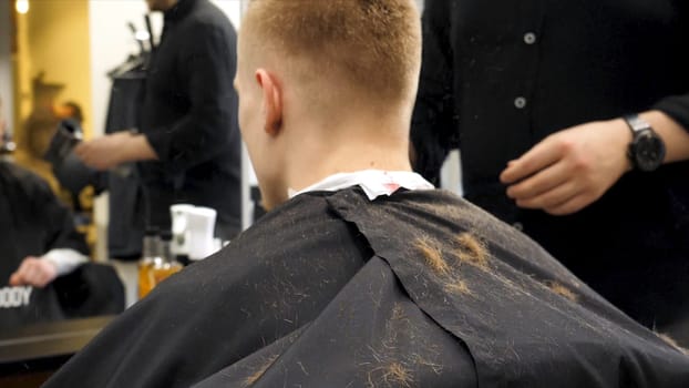 Barber cutting hair with scissors and hair flying in the air in slow motion. Back view of man in barber shop and flying hair in slow motion. Close-up back view of young bearded man getting beard haircut by hairdresser at barbershop