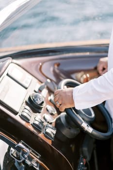 Captain steers a motor yacht with his hand on the steering wheel. Cropped. Faceless. High quality photo