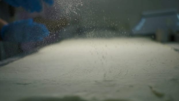 Close-up of sprinkling flour during cooking. Clip. Cook sprinkles flour on cooking table. Sprinkling flour for baking. Production bakery.