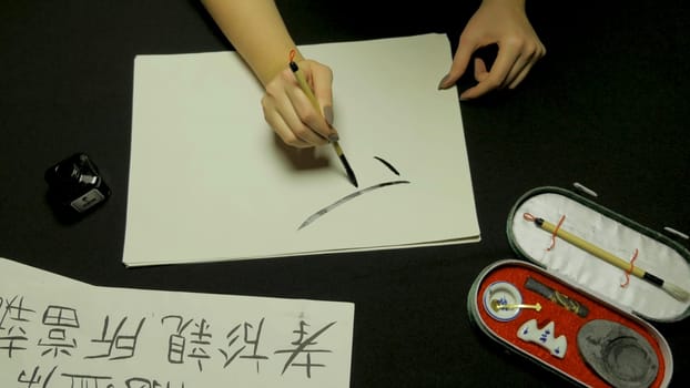 Woman's hand writing chinese calligraphy. Female hand holding a writing brush Chinese characters.