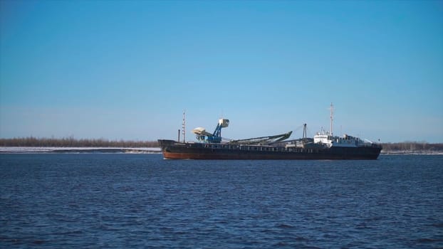 Cargo ship sailing on river on clear day. Clip. Merchant ship or barge sails along river. Commercial and industrial shipping.