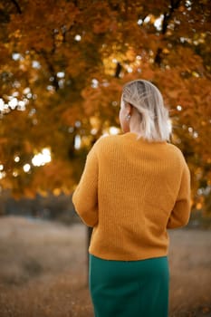 autumn woman in a yellow sweater and green skirt, against the background of an autumn tree.