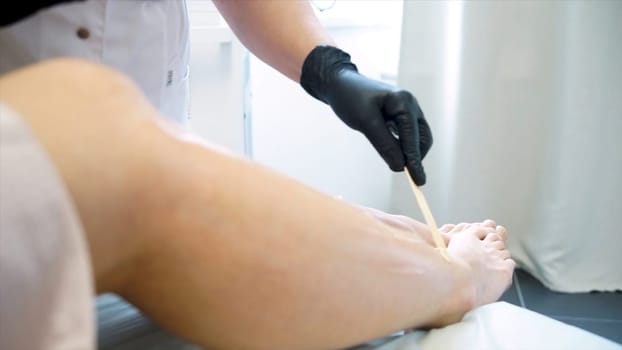 Close-up Of A Beautician Waxing Womans Leg In Beauty Spa. Process depilation female legs and hands in a beauty salon. Close up waxing in by a beautician in a spa center.