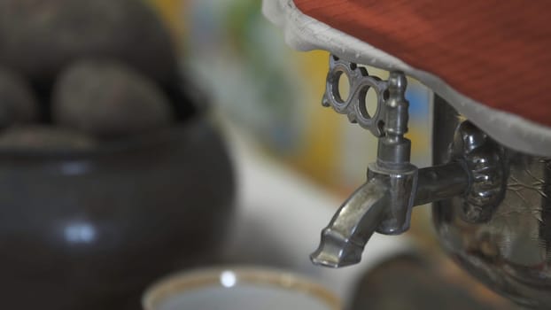 Close up of Russian teapot and a tea cup, russian traditions. Vintage, antique, shiny metal samovar details standing on the table.