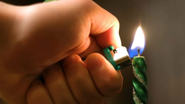 Close-up of man lighting Christmas candle. Concept. Man lights long holiday candle for cozy dinner on background of blurred lights.