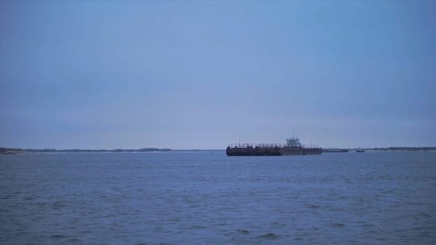Barge floating on river on cloudy day. Clip. Beautiful river landscape with floating merchant ship. Barge crossing on river on cloudy day.