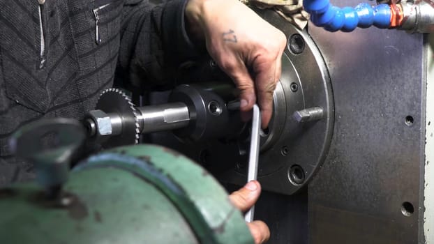 Mechanic repairman at the factory adjusting the machine with large and heavy key, holding it with both hands. Close up of machinery and professional equipment.
