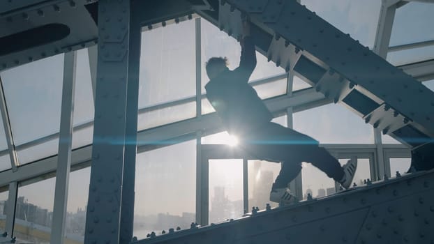 Young man dances on bridge on background of sun. Action. Young man is dancing on modern building structure.