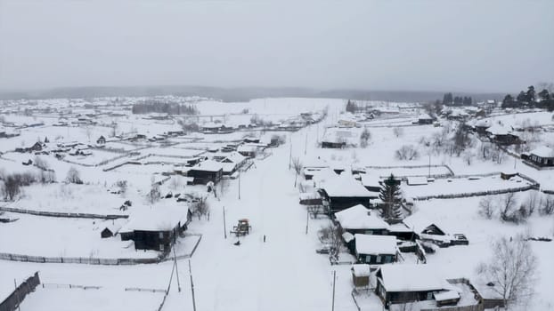 Aerial view of snow covered roofs of wooden houses. Clip. Small winter village on a heavy cloudy sky background