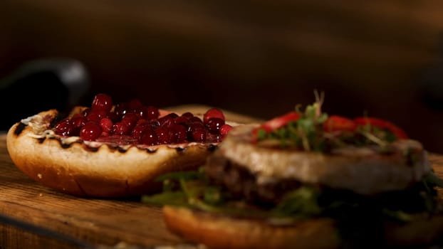 Close up of hamburger sandwich with cutlet of minced meat, cheese brie, camembert, berry cherry sauce. Male chef putting top burger bun on the other ingredients, foodporn and fast food concept.