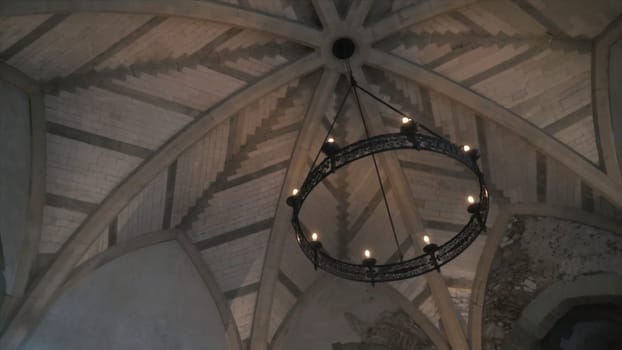View from the bottom on the old chandelier in the form of a wheel with light bulbs hanging on the ceiling in church or another old building. Beautiful retro style