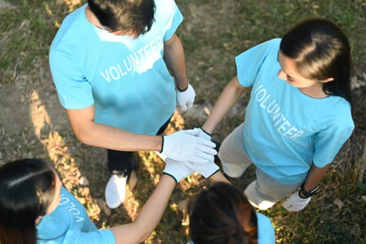 Overhead view young volunteers stacking hands together showing teamwork spirit. Charity and ecology concept.