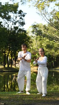 Full length view of active retired senior couple practicing traditional Tai Chi outdoors near lake