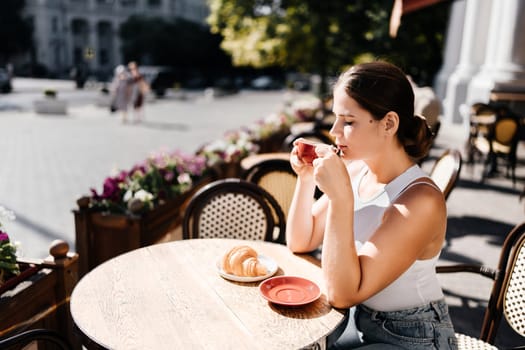 Portrait of happy woman sitting in a cafe outdoor drinking coffee. Woman while relaxing in cafe at table on street, dressed in a white T-shirt and jeans.