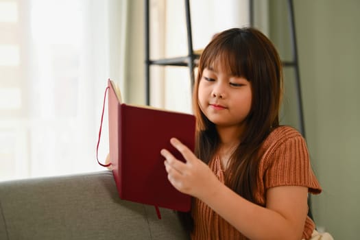 Happy Asian girl n casual clothes reading a book on couch at home